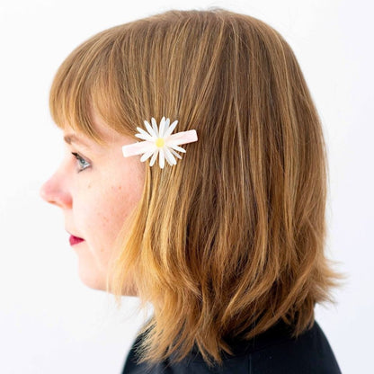 Person with a white hair clip featuring a yellow flower on a plain background