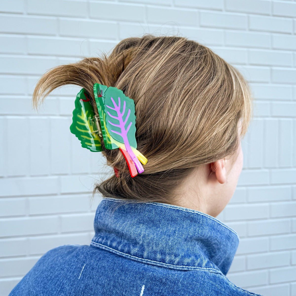 Person with colorful leaf-shaped hair clip in their hair against a light blue brick wall.