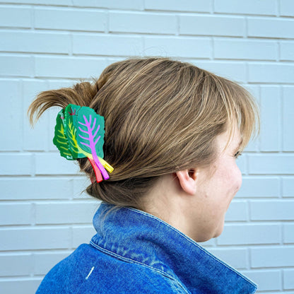 Person with a colorful hair clip in their hair against a light blue brick wall.