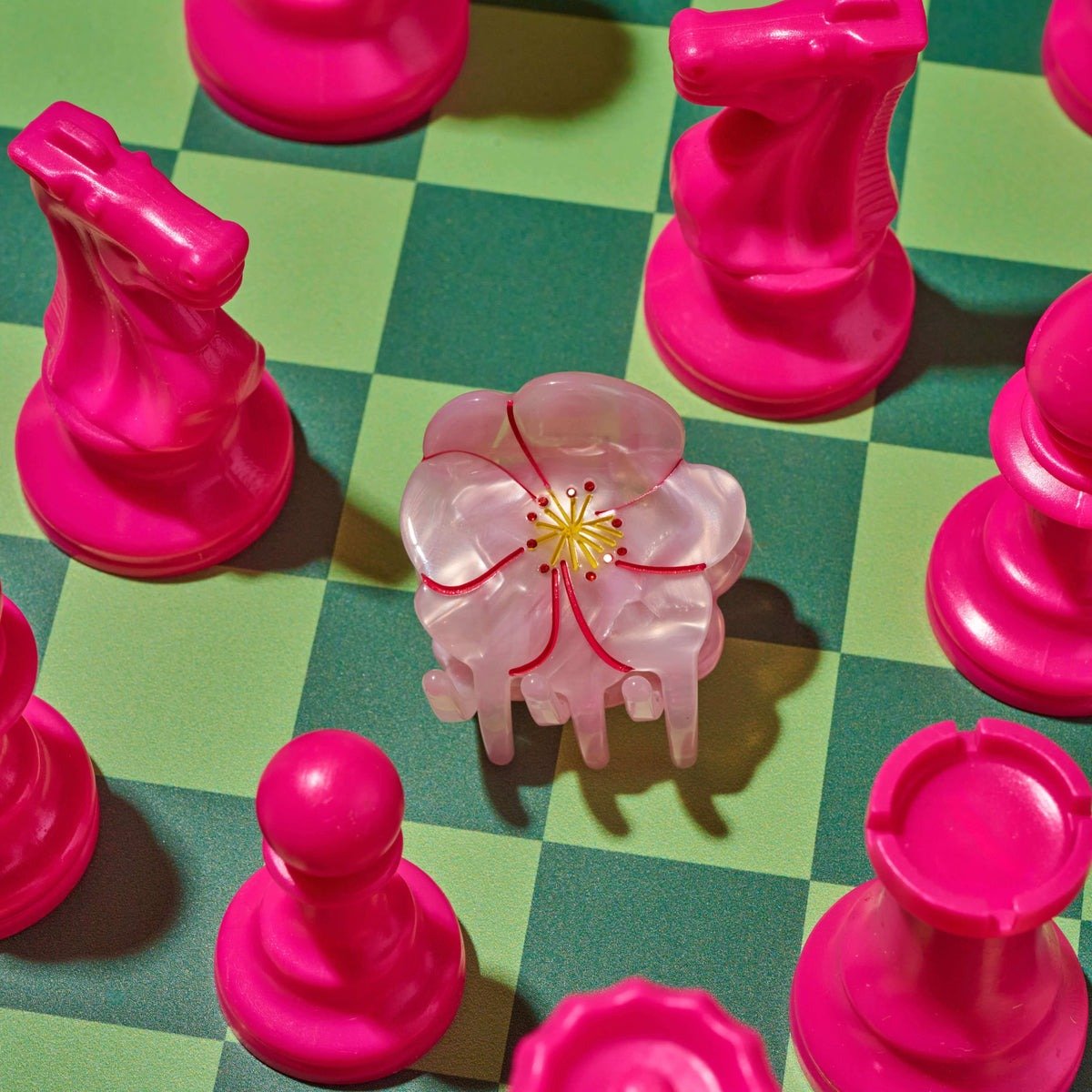 Pink chess pieces on a green checkered board with a central pink flower piece.