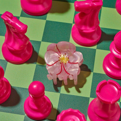 Pink chess pieces on a green checkered board with a central pink flower piece.