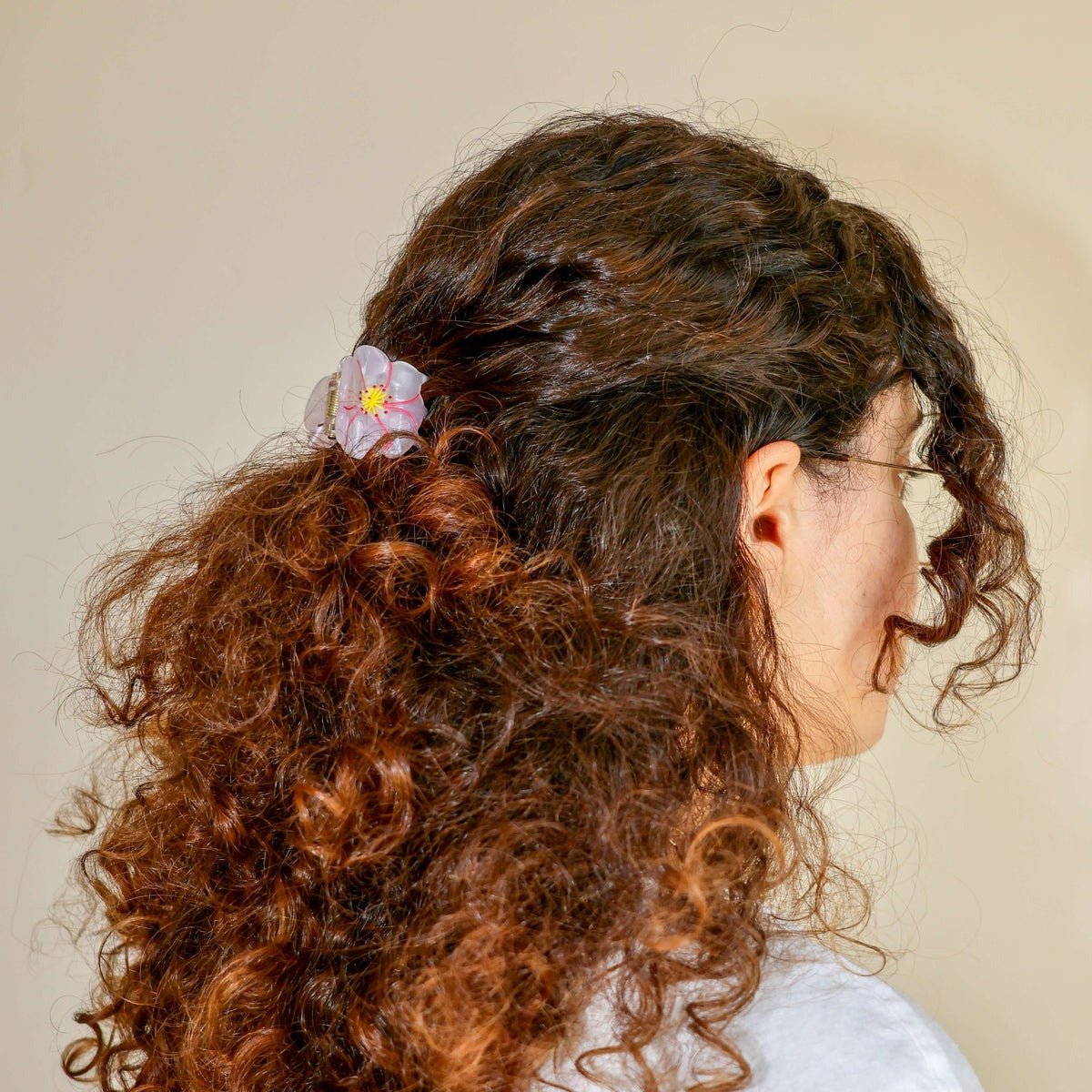 Person with curly hair wearing a floral hair clip against a neutral background
