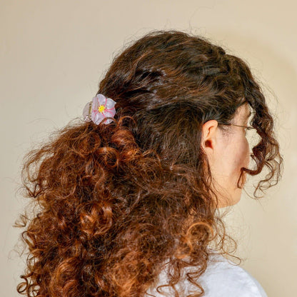 Person with curly hair wearing a floral hair clip against a neutral background