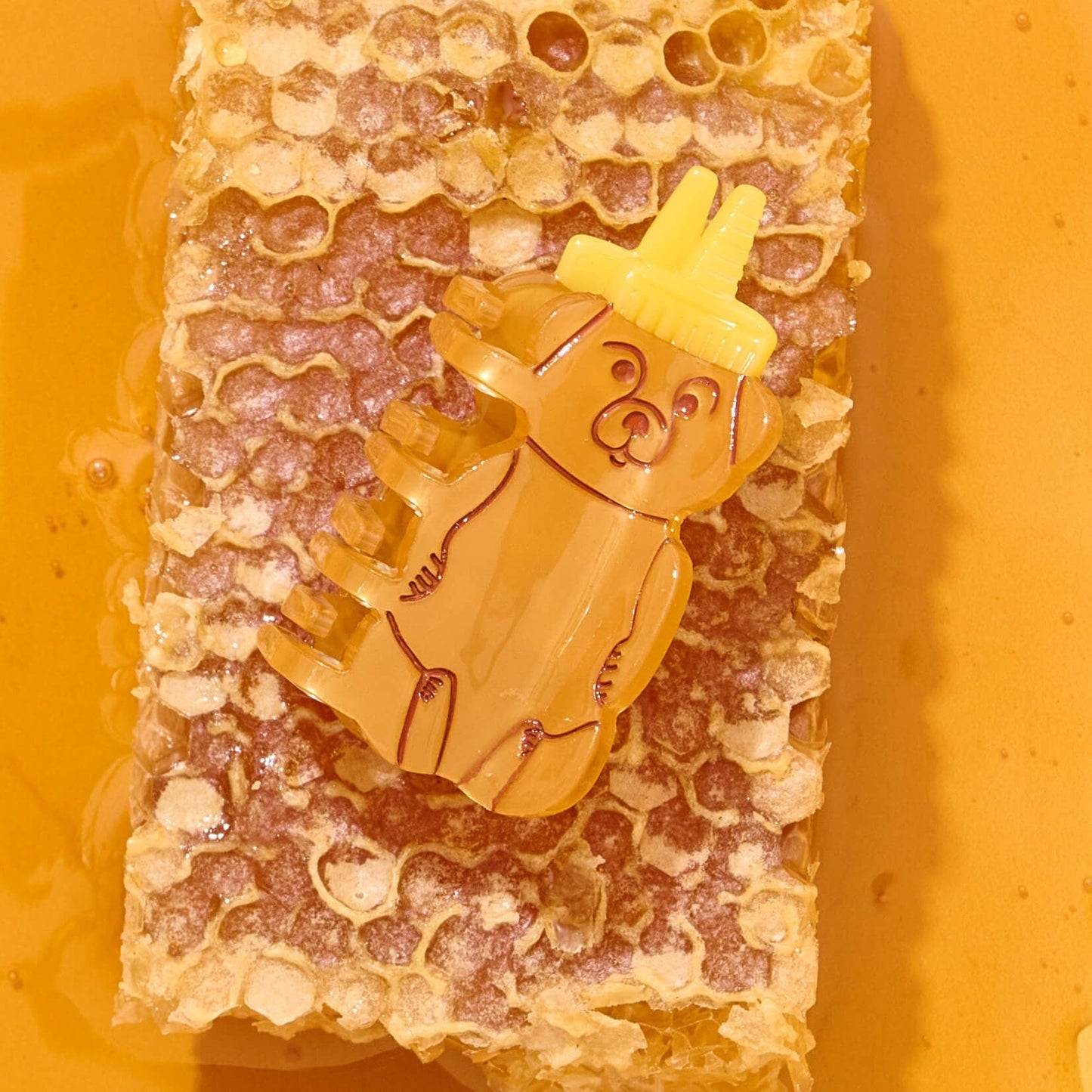 Yellow bear-shaped honey comb with a small yellow hat on a honeycomb background