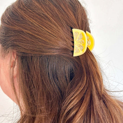 Person with brown hair wearing a yellow hair clip with decorative elements.