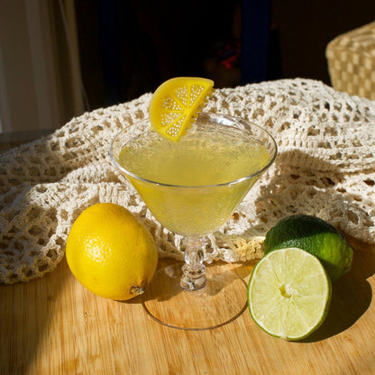 Cocktail in a martini glass with lemon and lime on a wooden surface