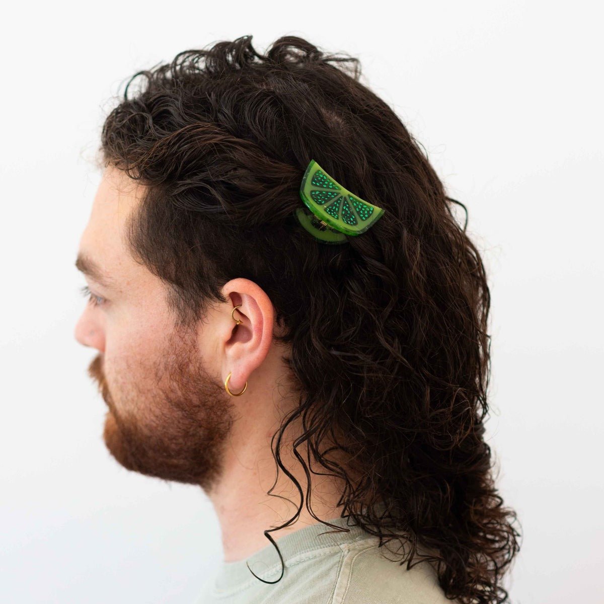 Man with curly hair wearing a green hair clip on a white background