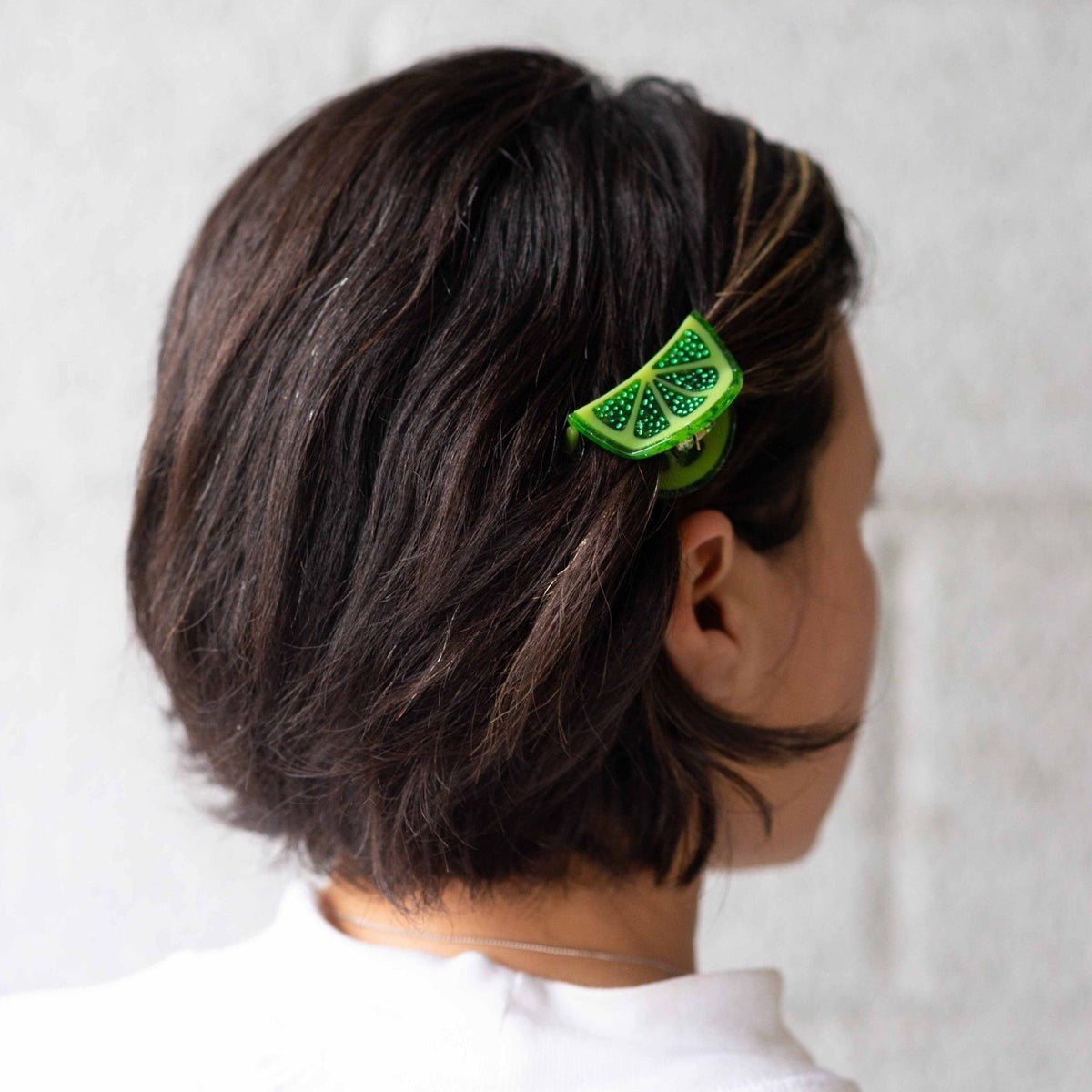 Person with a green decorative hair clip in their hair against a white background