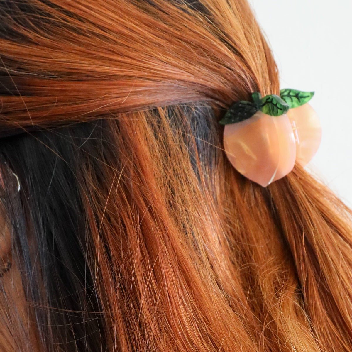 Hair tie shaped like a peach with green leaves in brown hair