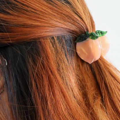 Hair tie shaped like a peach with green leaves in brown hair