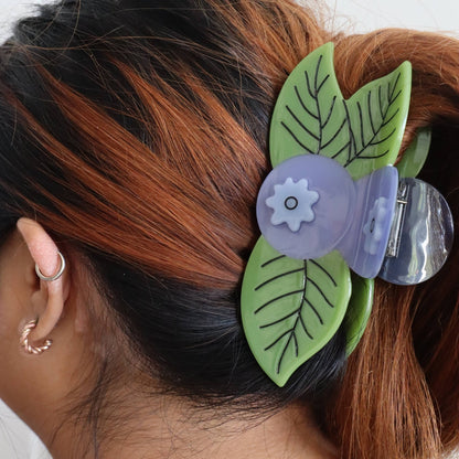 Hair clip with green leaves and a purple flower on a person's hair